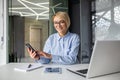 Portrait of a young business woman working in the office at a laptop, using a mobile phone and looking at the camera Royalty Free Stock Photo