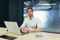 Portrait of young businessman with beard, man working in modern office with laptop smiling and looking at camera Royalty Free Stock Photo