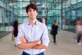 Portrait Of Young Businessman With Crossed Arms Standing In Lobby Of Busy Modern Office Royalty Free Stock Photo