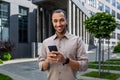 Portrait of young businessman, man smiling looking at camera holding phone, worker using app on smartphone while walking Royalty Free Stock Photo