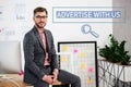 portrait of young businessman in suit and eyeglasses sitting on table in office advertise