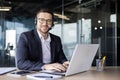 Portrait of a young businessman working in the office using a laptop and wearing a headset, smiling at the camera Royalty Free Stock Photo