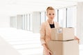 Portrait of young businesswoman carrying cardboard boxes in new office