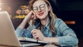 Portrait young businesswoman in fashionable glasses, sitting in cafe in front of computer and taking notes in notebook. Royalty Free Stock Photo