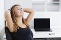 Portrait of young businesswoman with hands behind head sitting in front of desk in office Royalty Free Stock Photo