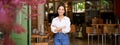 Portrait of young businesswoman in her own cafe, manager standing near entrance and inviting you, posing in white plain Royalty Free Stock Photo