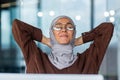 Portrait of a young businesswoman in hijab and glasses sitting in the office at the table in front of the computer. She Royalty Free Stock Photo