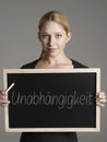 Portrait of young businesswoman holding blackboard with German text UnabhÃÂ¤ngigkeit (Independence)