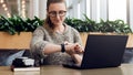 Portrait of young businesswoman sitting in cafe,working on laptop,looks at wrist watch. Online marketing, education.