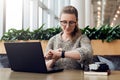 Portrait of young businesswoman sitting in cafe,working on laptop,looks at wrist watch. Online marketing, education. Royalty Free Stock Photo