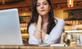 Portrait of young businesswoman, student, dressed in white blouse, sitting at table in cafe in front of computer.