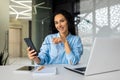 Portrait of young businesswoman at workplace, satisfied smiling woman smiling and looking at camera, holding phone Royalty Free Stock Photo