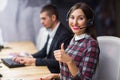 Portrait of young call center operator wearing headset with colleagues working in background at office Royalty Free Stock Photo