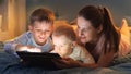 Portrait of young caring mother with two sons using tablet computer in bed before going to sleep. Family having time together, Royalty Free Stock Photo