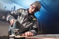 Portrait of a young carpenter joiner with electric jigsaw in the hands of a worker in a home workshop. Starting a