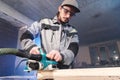 Portrait of a young carpenter working with an electrical plane in a home wood workshop. The concept of a business idea