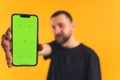 Portrait of young Caucasian bearded man in a black t-shirt showing green screen of his smartphone at the camera. studio Royalty Free Stock Photo