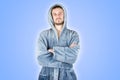 Portrait of young caucasian bearded man in blue bathrobe with crossed hands isolated on blue background Royalty Free Stock Photo