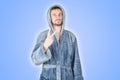 Portrait of young caucasian bearded man in blue bathrobe shows victory or peace gesture isolated on blue background