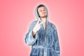 Portrait of young caucasian bearded man in blue bathrobe shows victory or peace gesture isolated on pink background