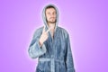 Portrait of young caucasian bearded man in blue bathrobe shows victory or peace gesture isolated on purple background