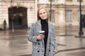 Portrait of a young Caucasian blonde girl who smiles and drinks coffee with pleasure in the shade in the city. Royalty Free Stock Photo