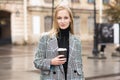 Portrait of a young Caucasian blonde girl who smiles and drinks coffee with pleasure in the shade in the city. Royalty Free Stock Photo