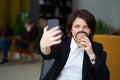 Portrait of young caucasian business woman wearing black suit doing selfie on the phone while coffee break Royalty Free Stock Photo