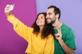 Portrait of young caucasian couple in colorful clothing showing peace fingers while taking selfie photo on cellphone Royalty Free Stock Photo