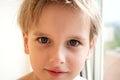 Portrait young caucasian cute boy with blond hair inside the house near the window. Calm emotion Royalty Free Stock Photo