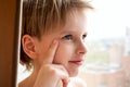 Portrait young Caucasian cute boy with blond hair inside the house near the window. Pensive emotion Royalty Free Stock Photo