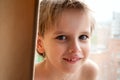 Portrait of a young Caucasian cute boy with blond hair inside the house near the window. A smiling, cheerful emotion Royalty Free Stock Photo