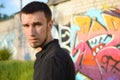 Portrait of young caucasian graffiti artist in black t-shirt near colorful pink graffiti on brick wall. Street art and Royalty Free Stock Photo