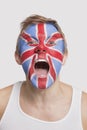 Portrait of young Caucasian man with British flag painted on face cheering against white background Royalty Free Stock Photo