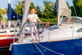 Portrait of young Caucasian white girl on prow of sailboat or yacht anchored in marina at bright sunny day Royalty Free Stock Photo