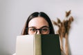 Portrait of young caucasian woman college student in eyeglasses hiding behind a book and looking at camera Royalty Free Stock Photo