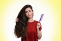 Portrait of a young caucasian woman holding her thick dark hair and comb for combing. White and yellow background. Copy space.