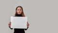 Portrait of young caucasian woman looking at camera, holding white blank banner in front of her while standing isolated Royalty Free Stock Photo