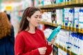 A portrait of young Caucasian woman in a red sweater holds a bottle of shampoo and reads the ingredients on the label. In the