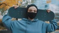 Portrait of young caucasian woman skater with protective face mask holding skateboard behind her head in the park in Royalty Free Stock Photo