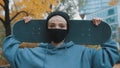 Portrait of young caucasian woman skater with protective face mask holding skateboard behind her head in the park in Royalty Free Stock Photo