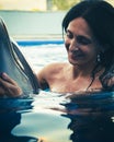 Portrait of young Caucasian woman smile with dolphin in pool water of Batumi delphinarium. Swim with dolphin experience concept