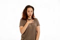 Portrait of a young Caucasian woman in surprise, putting her hand on her chest. White background. The concept of surprise