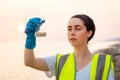 Portrait of young Caucasian woman wearing protective gloves and vest, holds research sample flask. Ecologist examines