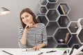 Portrait of young cheerful dark-haired female freelance designer sitting at table in comfy co-working space, doing work