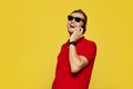 Portrait of a young cheerful man wearing red polo shirt and sunglasses having phone call on yellow backdrop. Royalty Free Stock Photo