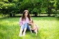 Portrait of a young cheerful woman sitting in the park on the green grass with a dog from the shelter. Royalty Free Stock Photo