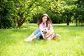 Portrait of a young cheerful woman sitting in the park on the green grass with a dog from the shelter. Royalty Free Stock Photo