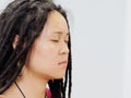 Portrait of young Chinese female with cute dreadlocks and thoughtful face sitting and meditating with eyes closed