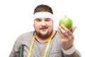 Portrait of young chubby man with measuring tape holding apple